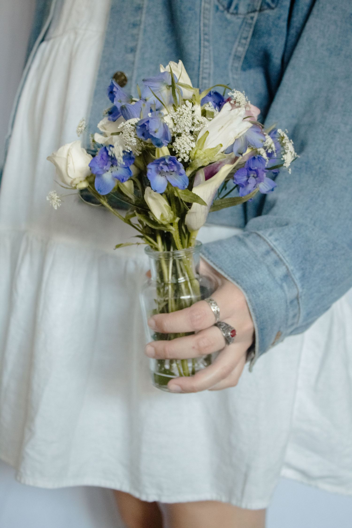 Delicate bouquet of white roses and purple iris flowers held against white and denim clothing.