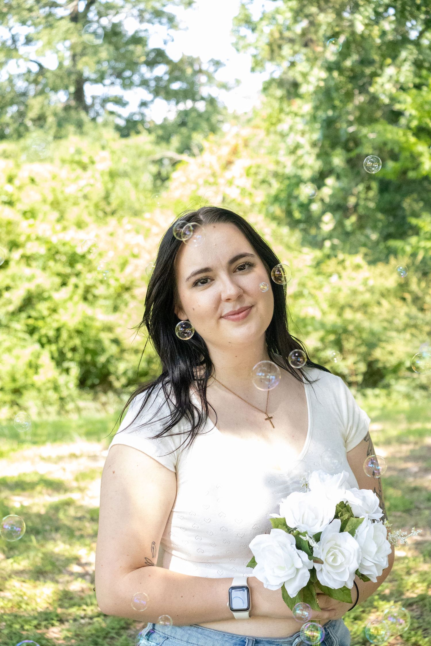 Woman in white top holds a bouquet of white roses in a sunny outdoor garden setting.