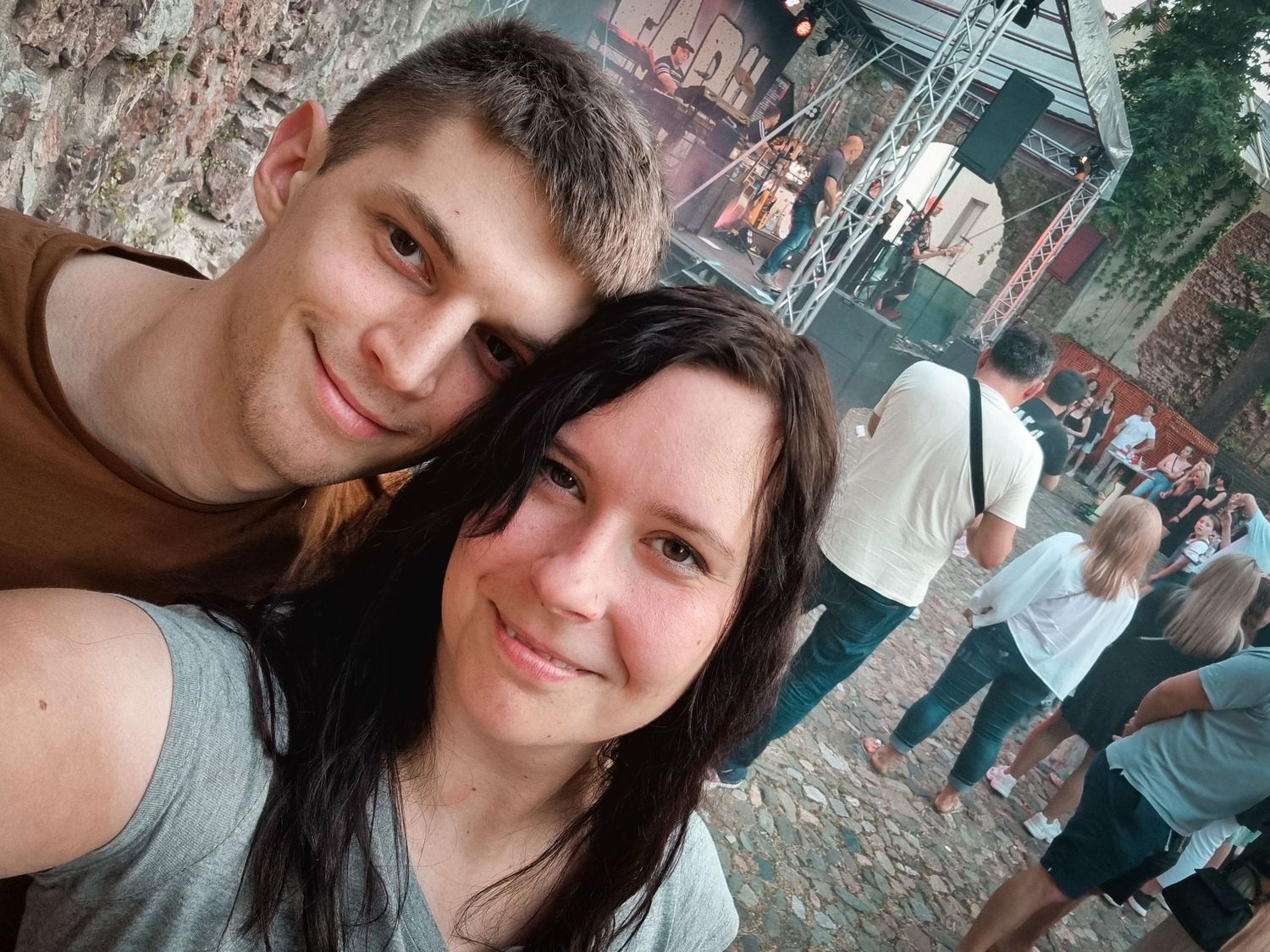 Par na rock koncertu, selfie pred odrom, sproščeno vzdušje, glasba v ozadju in nasmejana obiskovalca v ospredju.