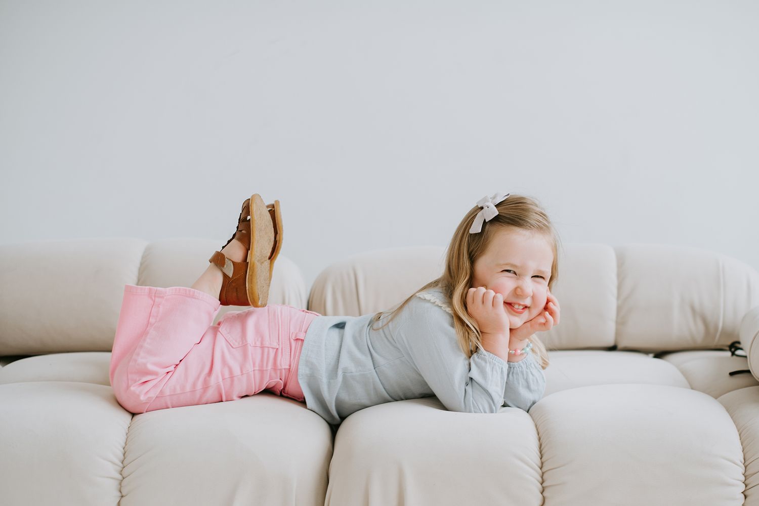 Person relaxing and stretching out on a cozy beige sofa with pink and gray throw pillows in a bright living room.