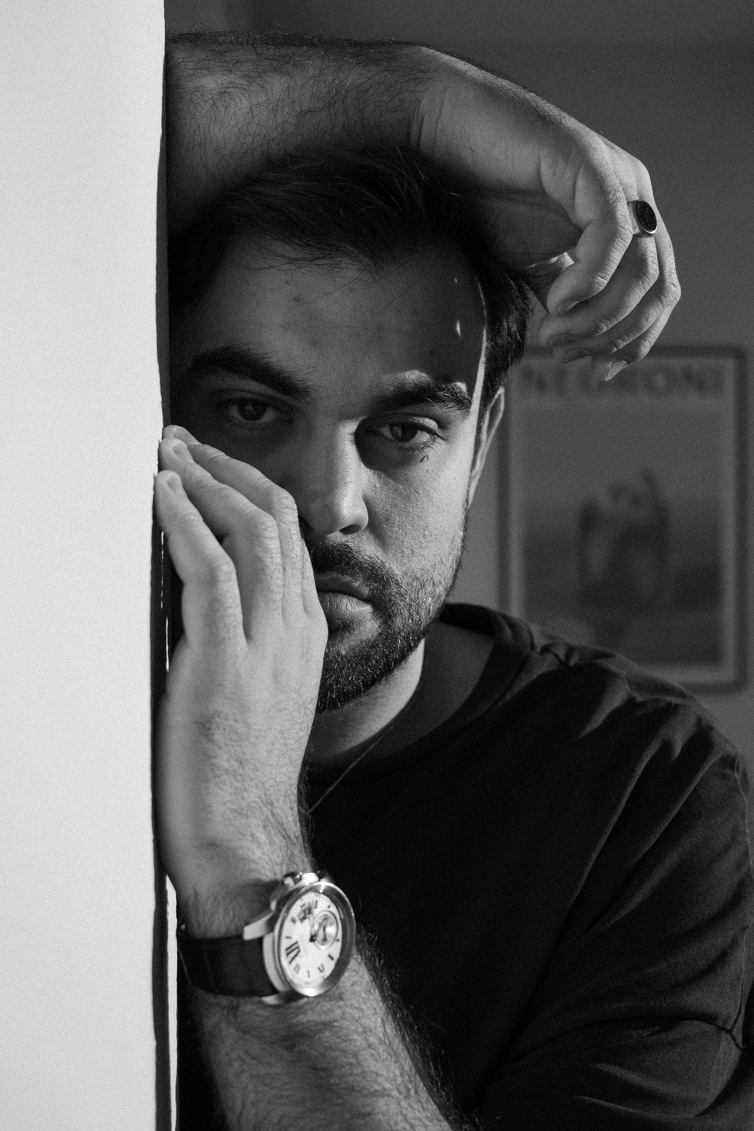 A dramatic black and white portrait of someone in a dark shirt wearing a watch, resting their face against their hand.