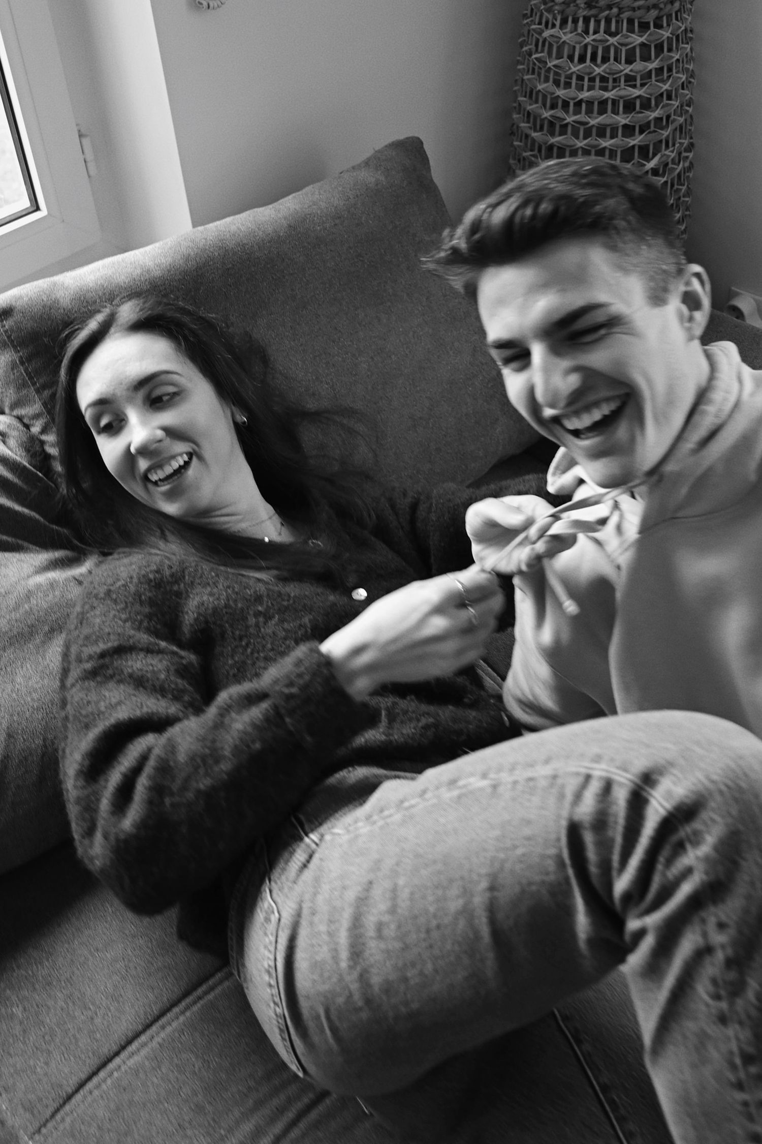 A relaxed moment of laughter shared on a cozy couch in black and white.