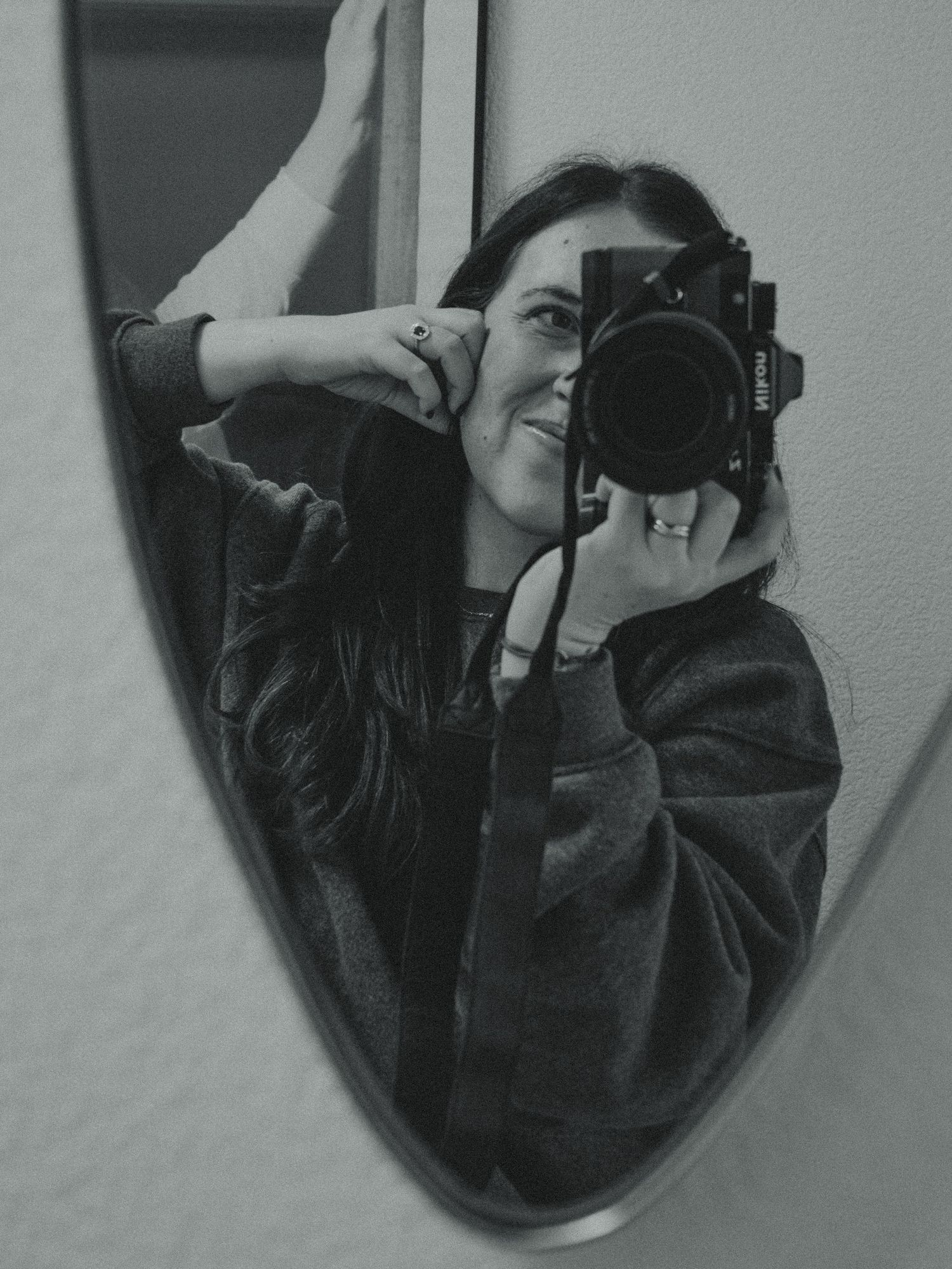 Black and white mirror selfie of someone taking a photo with professional camera and smiling.