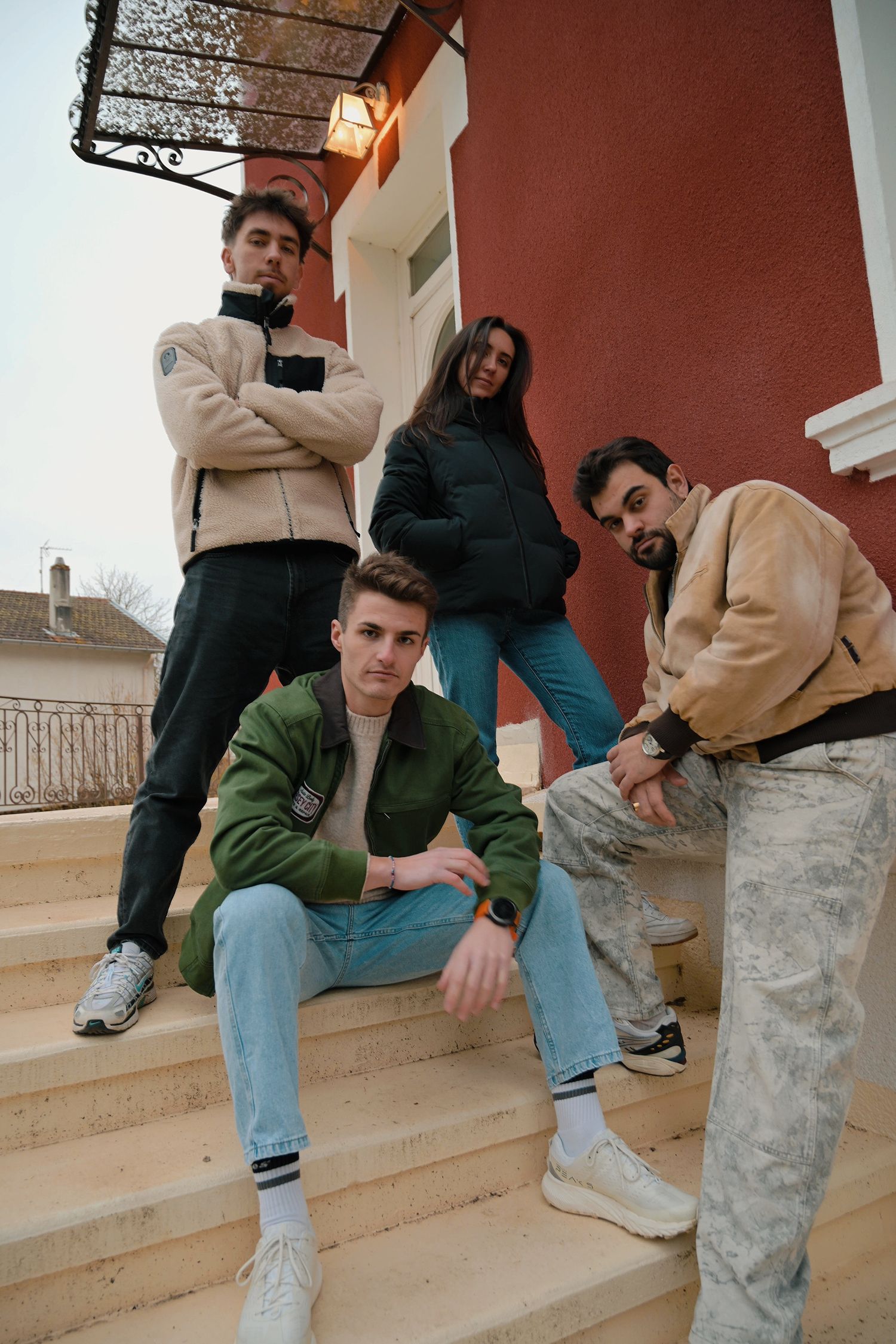 Group of four friends in casual wear posing on concrete steps outside building.