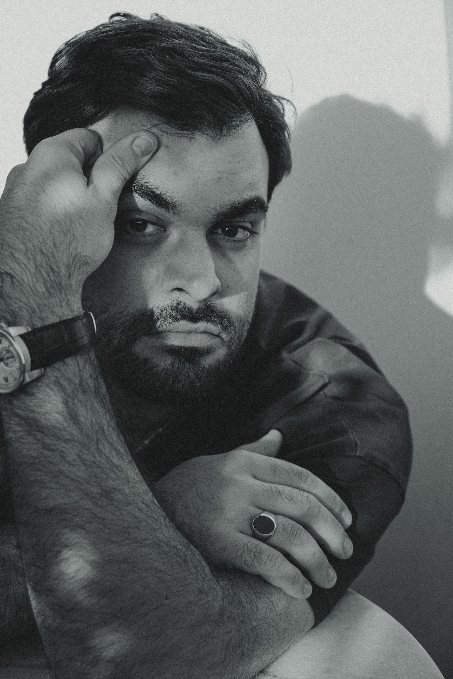 Black and white portrait photograph showing thoughtful expression with hand resting against head while wearing dark attire.
