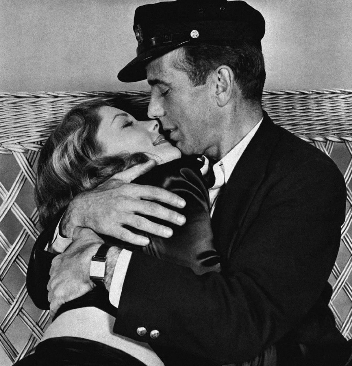 A romantic black and white photograph shows a tender embrace between two people on wicker furniture.