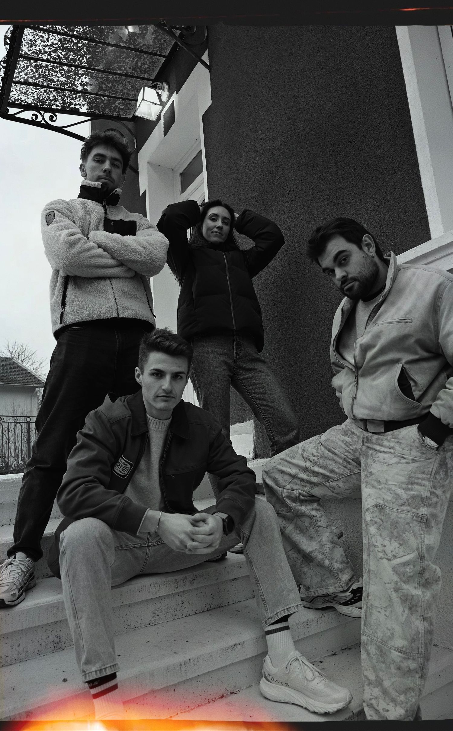 Group of young people in casual wear standing and sitting on concrete steps in black and white photography.