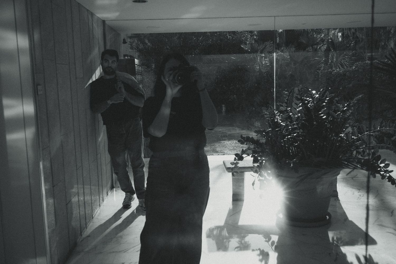 Black and white photo of silhouetted figures in hallway with dramatic lighting and shadows cast on floor.