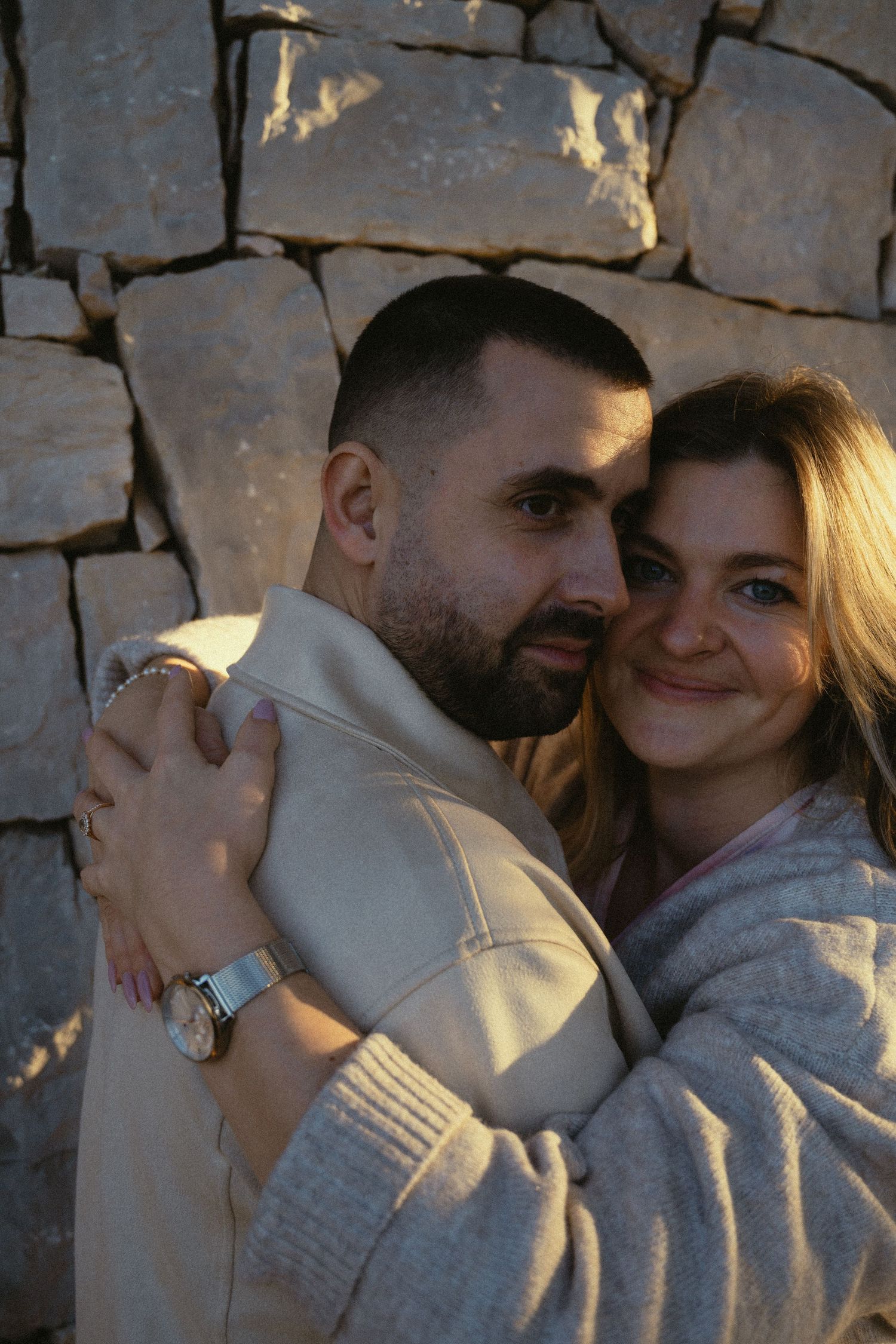 An intimate moment shared against a stone wall background during golden hour.