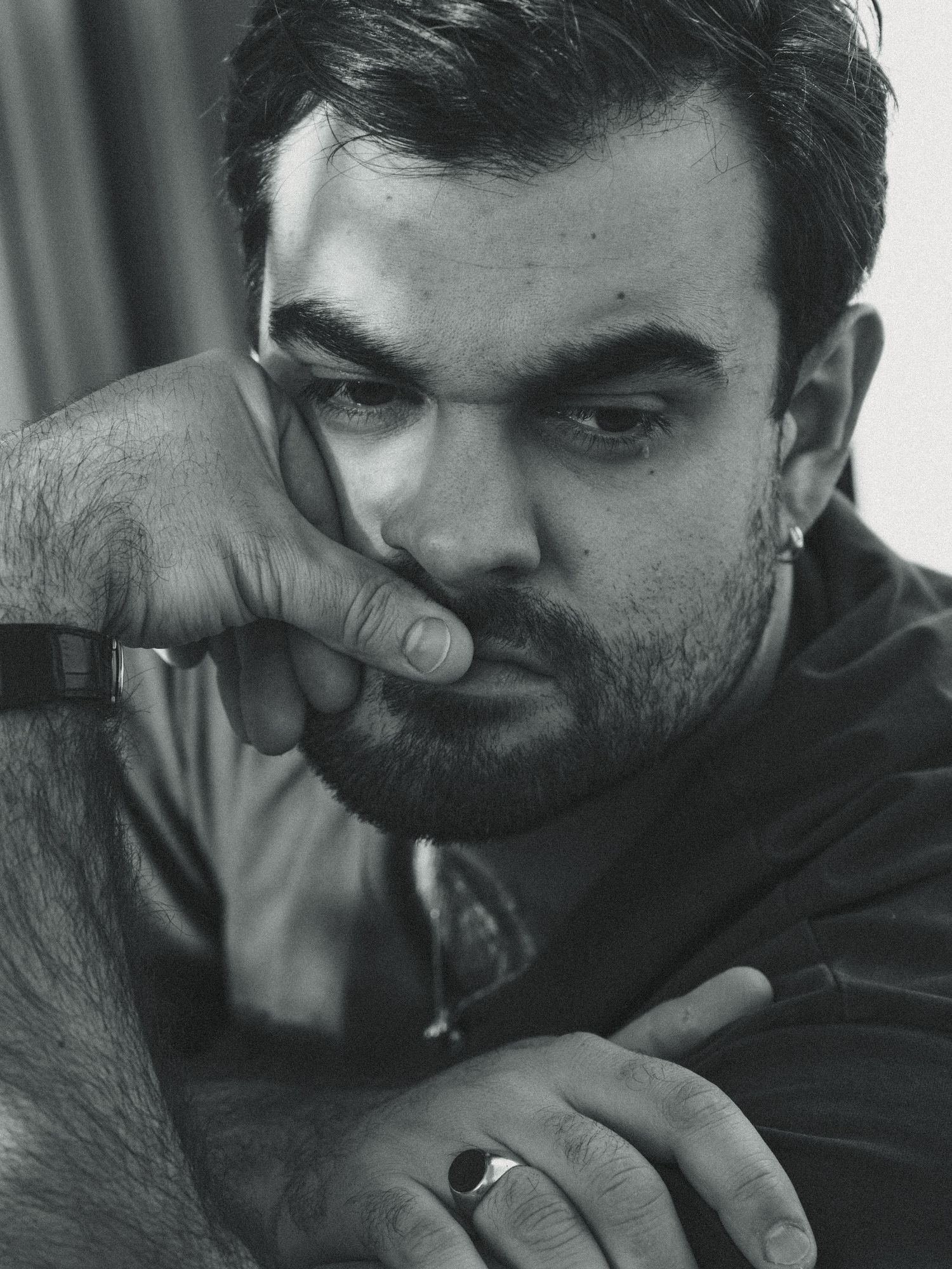 Black and white portrait photograph of a person with a beard in contemplative pose resting fingers near their mouth.