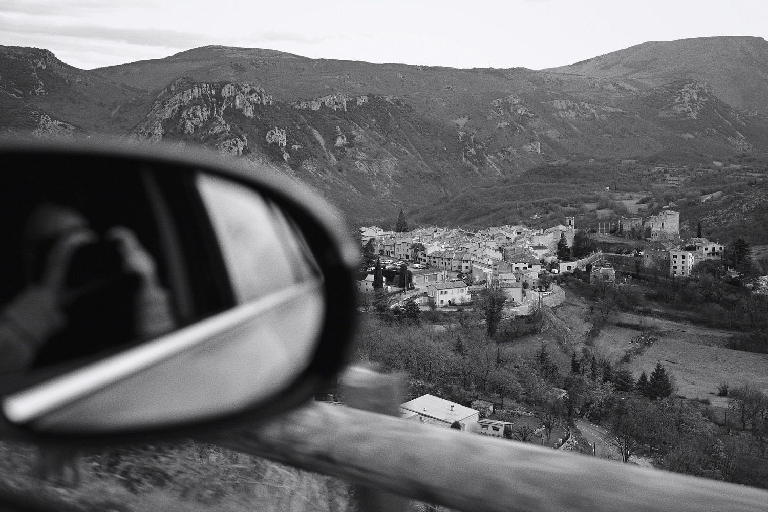 Black and white landscape view of a mountain village through a car side mirror.