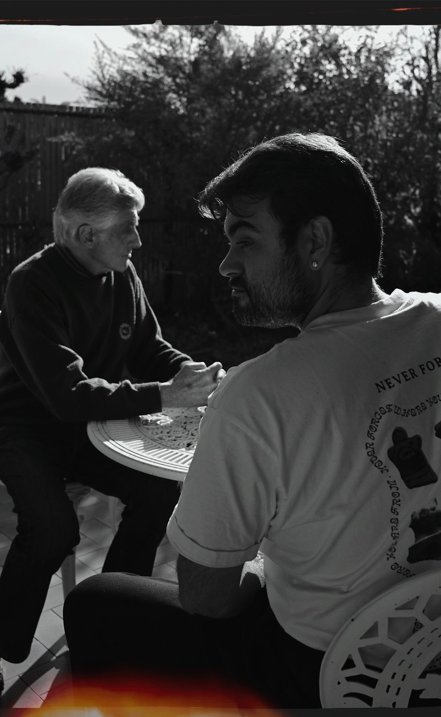 Two people engaged in conversation at outdoor table in moody black and white composition.