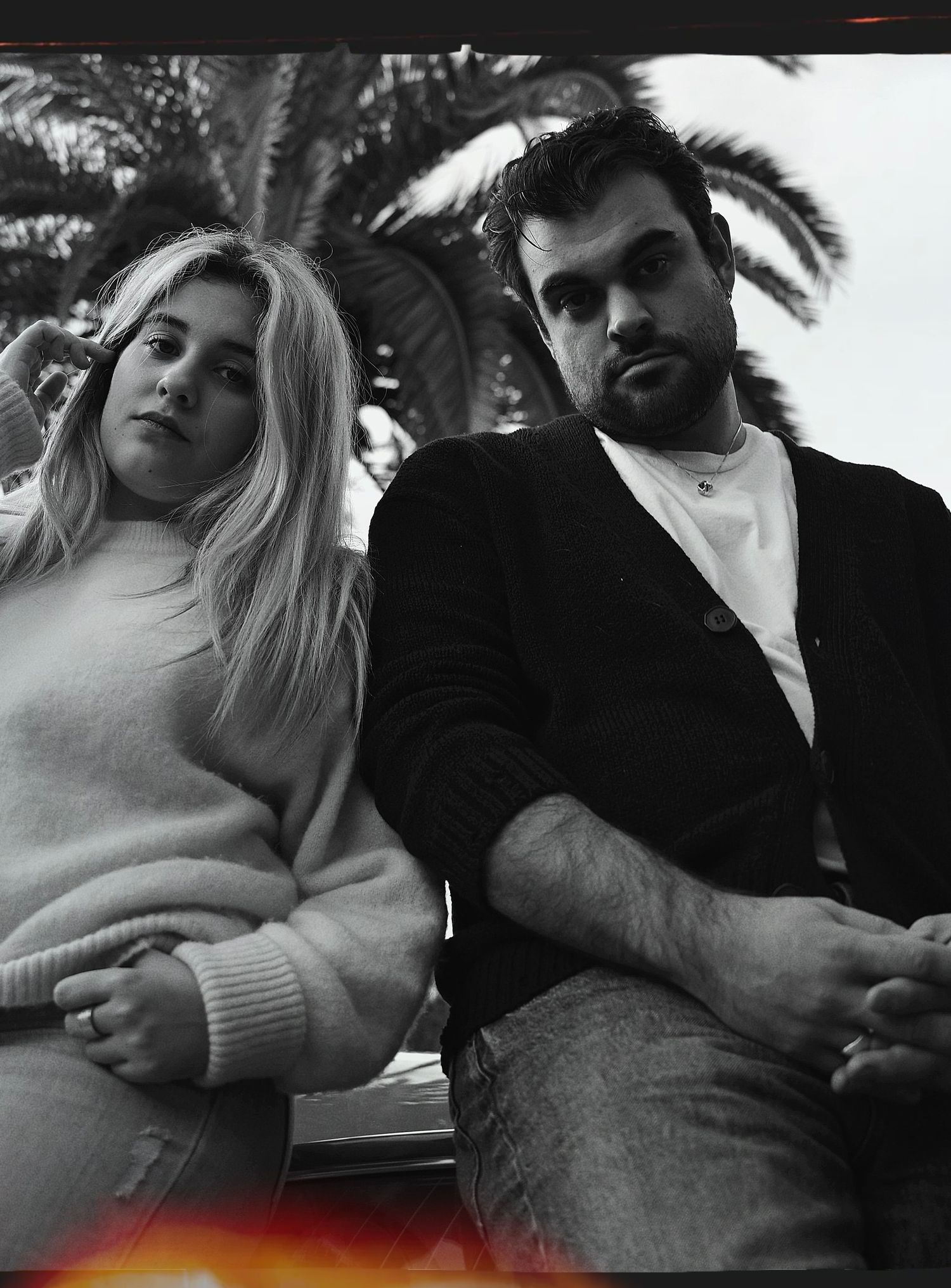 Family in casual sweaters posed against palm tree background in black and white portrait.