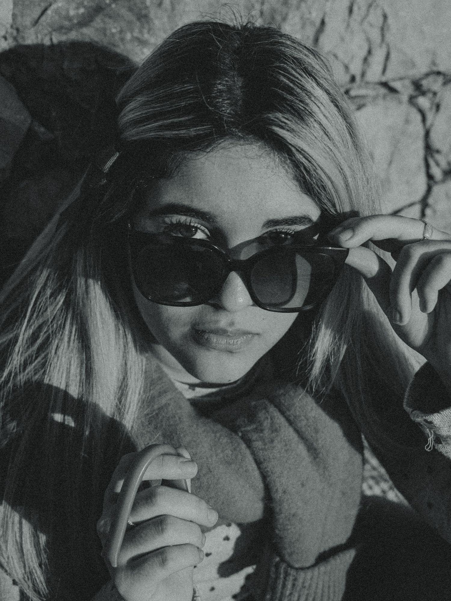 A black and white portrait photograph showing someone in sunglasses and a sweater looking at the camera with a slight smile.