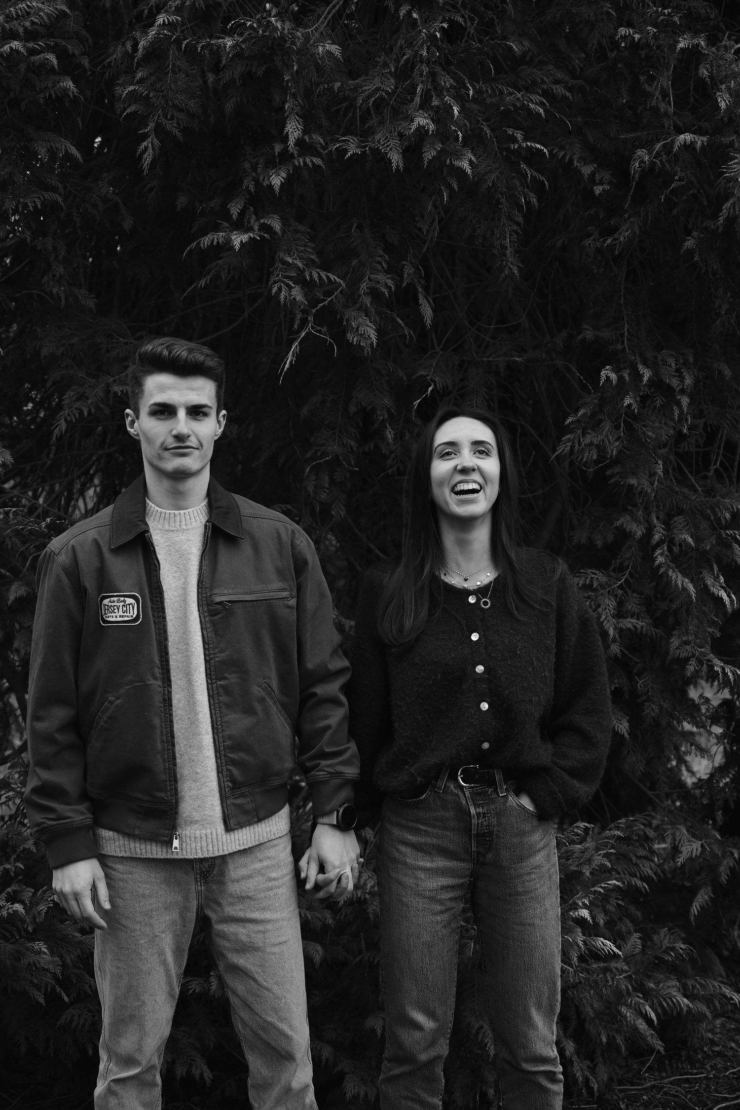 A smiling couple standing together against a leafy background in monochrome.