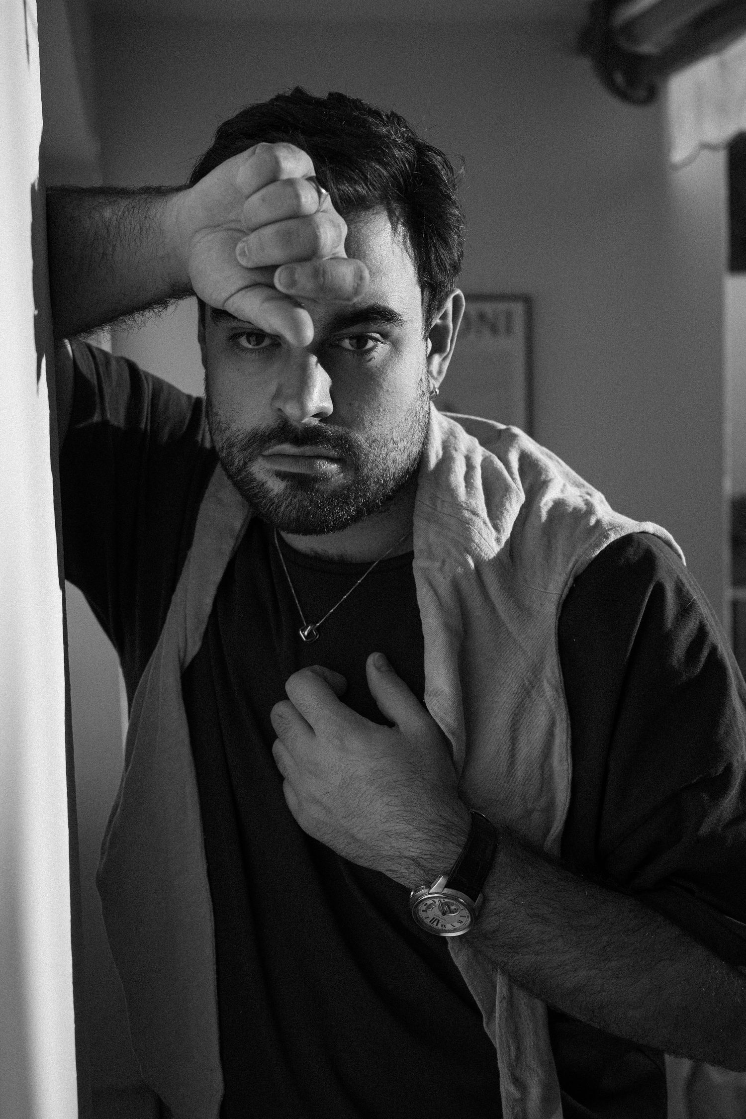 A dramatic black and white portrait shows a person with dark hair wearing a necklace and casual shirt in moody lighting.