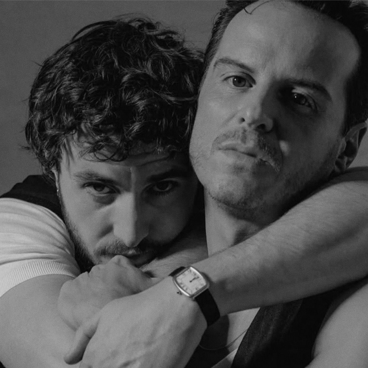 Black and white portrait of two men posing closely together, with one wearing a white shirt and a watch.