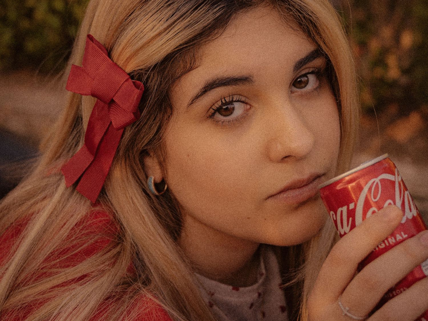 Close up portrait view with blonde hair and red bow holding a Coca Cola can in warm autumn lighting.