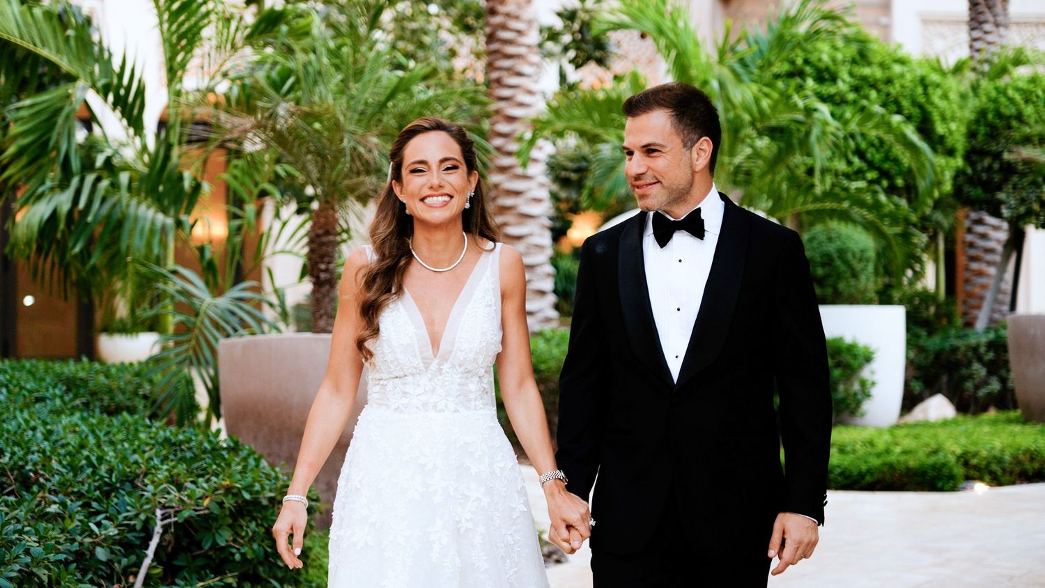 A couple in formal wedding attire walk hand in hand through a lush tropical garden setting with palm trees.
Dubai Wedding at Four Seasons -