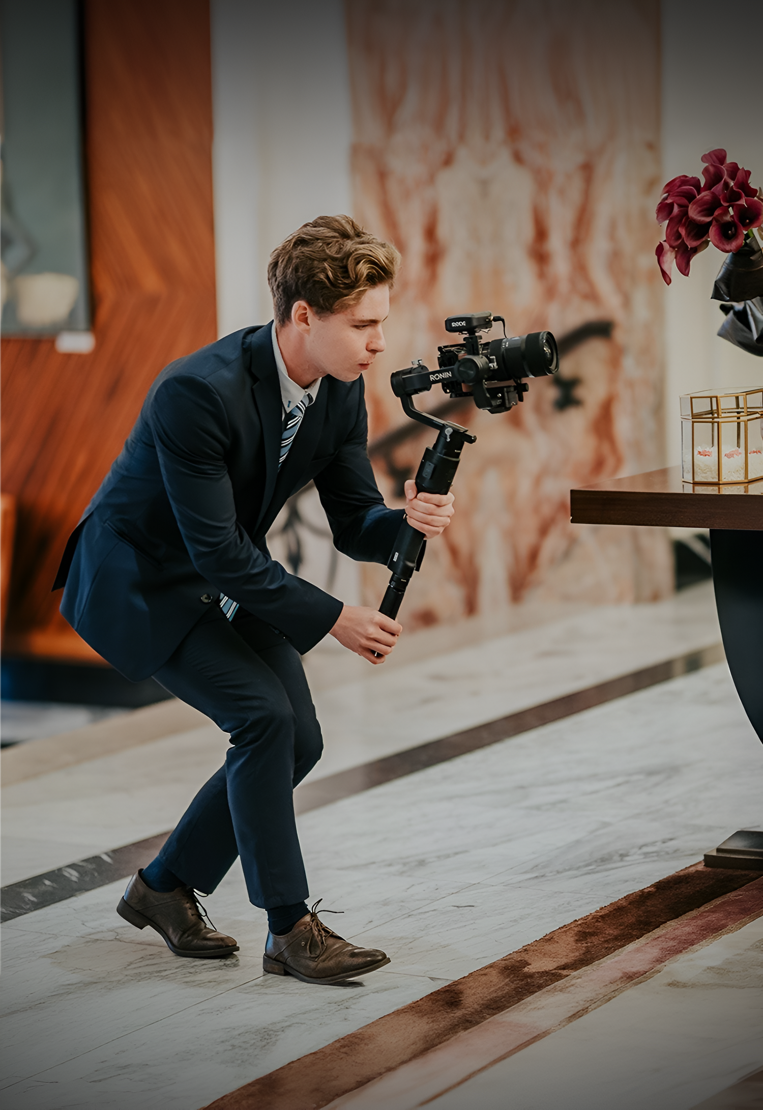Professional photographer in navy suit crouches low to capture creative angle while shooting with DSLR camera.