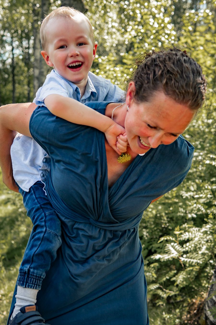 Ett lekfullt ögonblick utomhus då ett barn rider på sin mammas rygg med träd i bakgrunden. Fotograf, Familjefotograf, Umeå