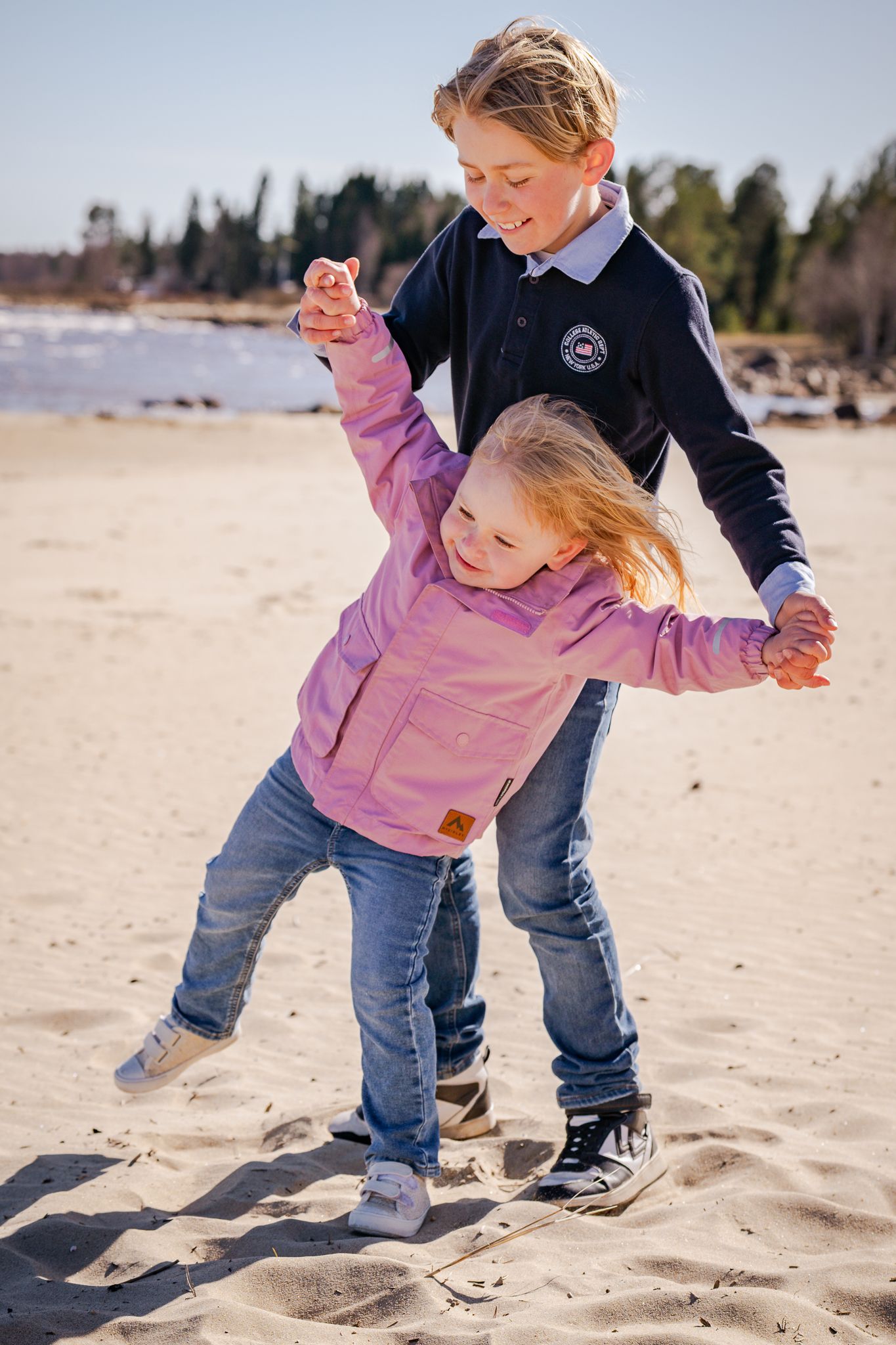 Lekfull bild med syskon som håller varandras händer på sandstranden en solig dag. Fotograf, familjefotograf, Umeå, Västerbotten