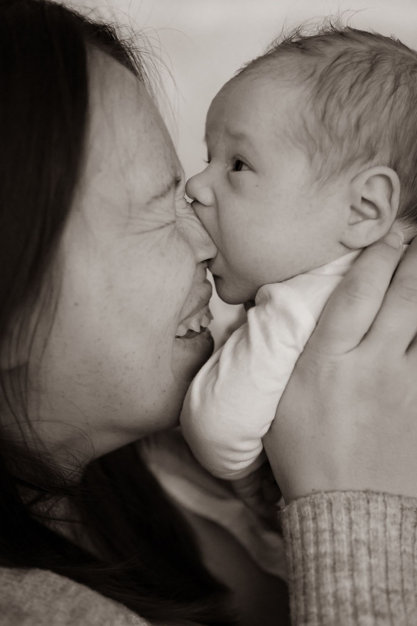 Svartvit bild på ett nära ögonblick mellan mamma och nyfödd där bebis slickar på mammas näsa. Fotograf, nyföddfotograf, Umeå, Västerbotten