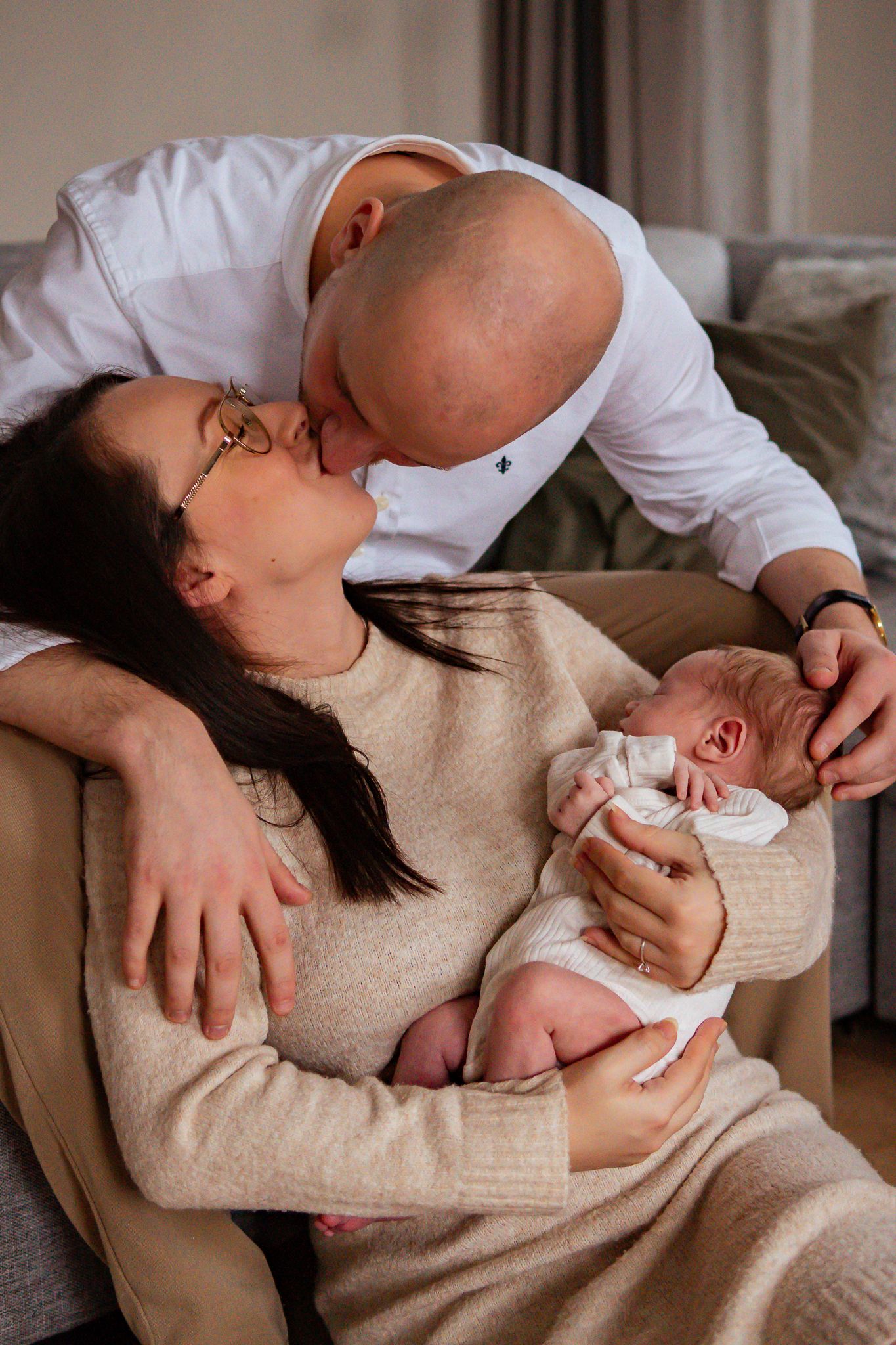 Föräldrar pussas när mamma sitter på golvet framför pappa, och mamma håller nyfödda bebisen i famnen. Fotograf, nyföddfotograf, Umeå