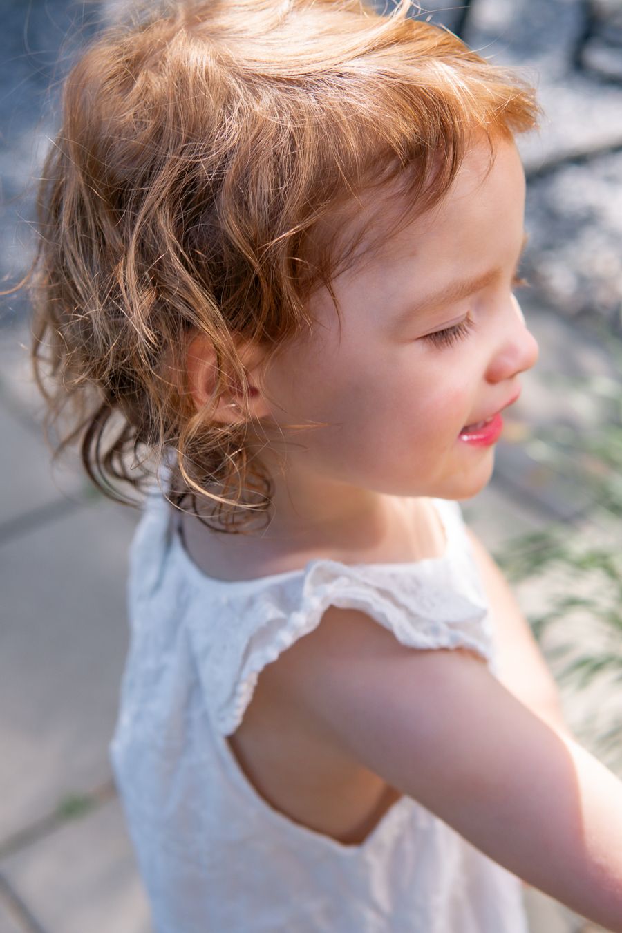 Profil av en liten flicka som ler och tittar bort i vit sommarklänning och lockigt orange hår. Fotograf, nyföddfotograf, Umeå, Västerbotten