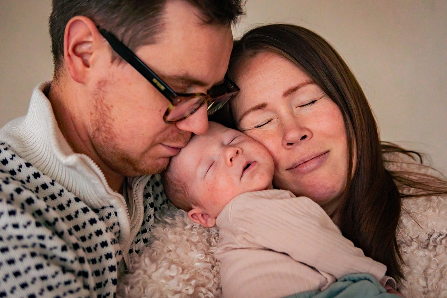 Mysig stund med två föräldrar som kärleksfullt håller sin nyfödda bebis tätt intill i famnen, allas huvuden nuddar varandra. Fotograf, Umeå