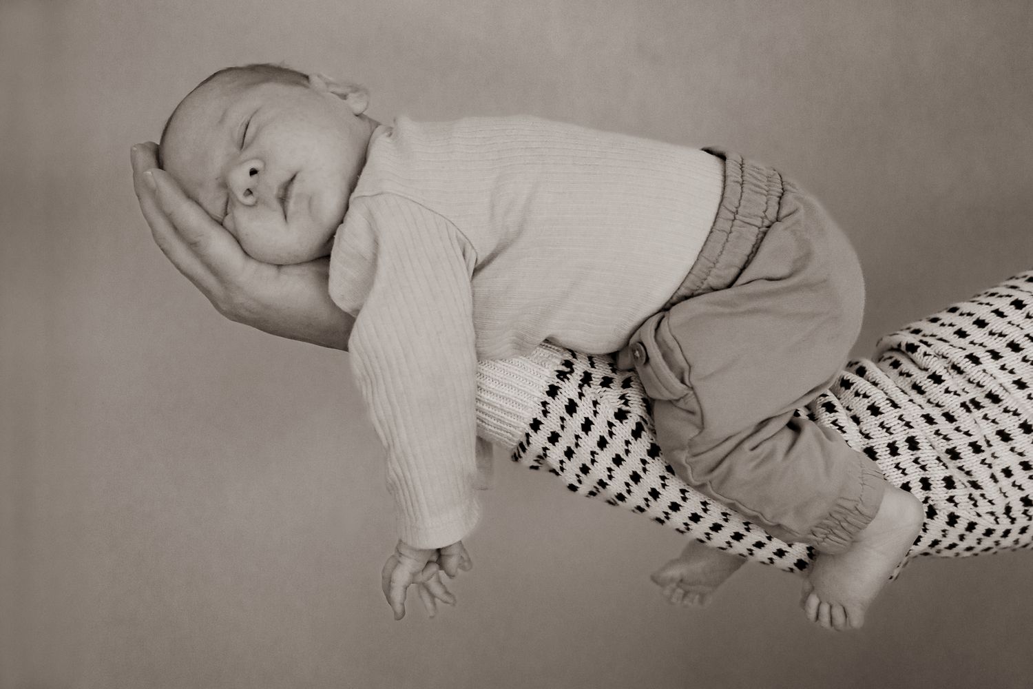 Svartvit bild på en sovande bebis som ligger på pappas underarm med huvudet i handen. Nyföddfotograf, Umeå, Västerbotten