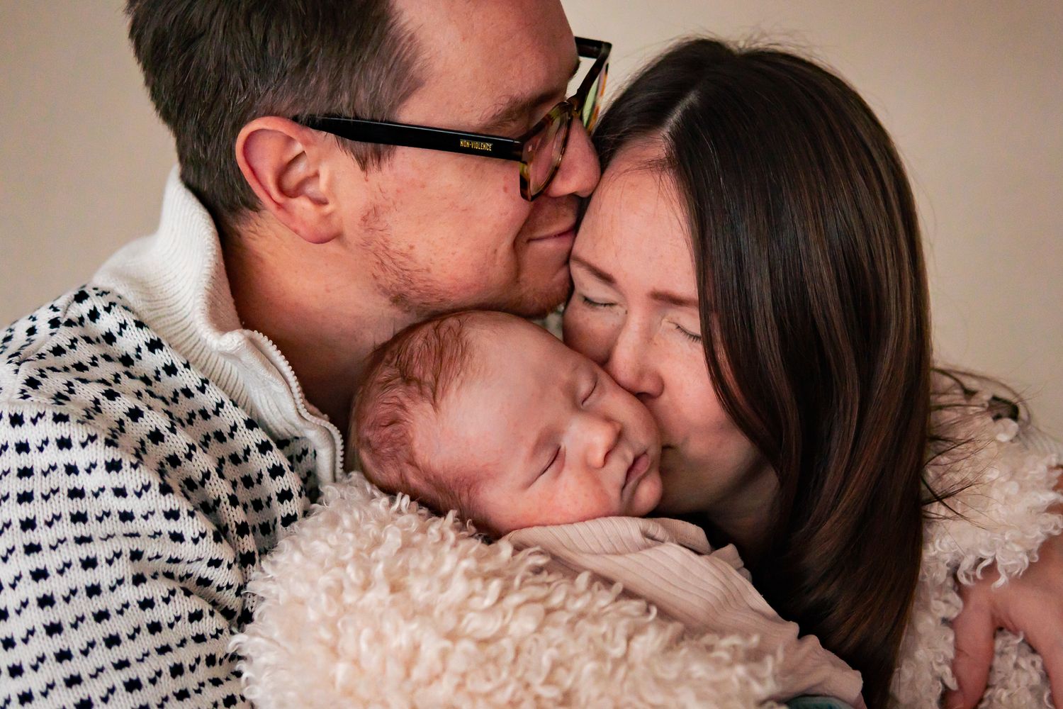 Föräldrar med en sovande bebis i famnen står kärleksfullt tätt intill varandra med ansiktena. Fotograf, nyföddfotograf, Umeå