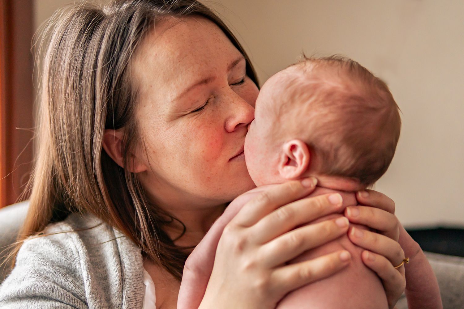 Kärleksfull stund mellan mamma och nyfödd där de delar en puss i varmt naturligt ljus. Fotograf, nyföddfotograf, Umeå, Västerbotten