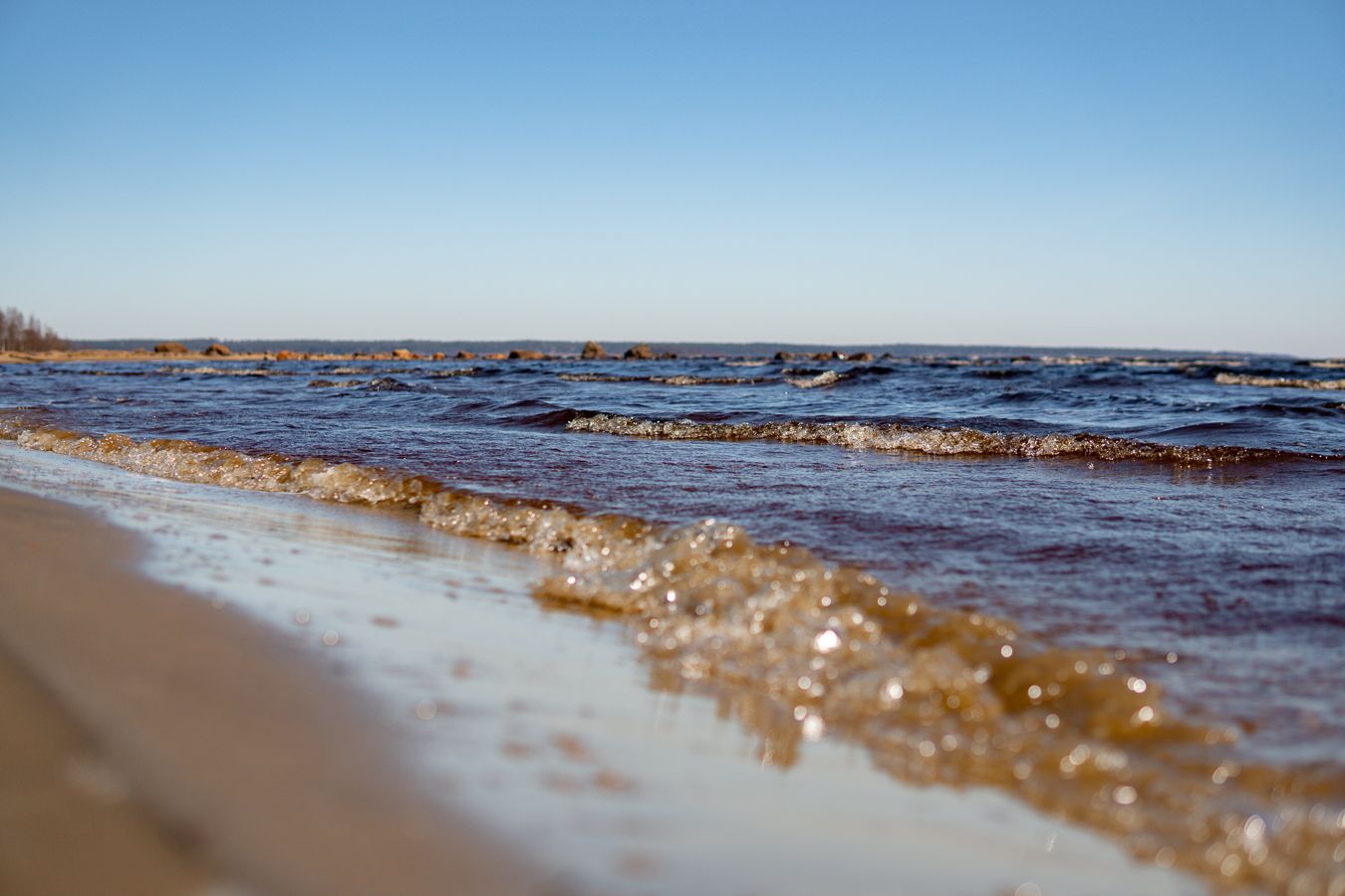 Close-up of gentle waves lapping at sandy beach shore during daytime.