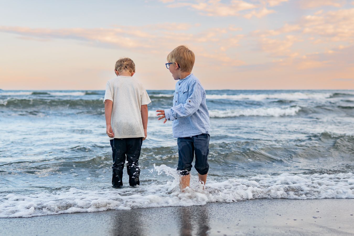 Två barn leker med kläderna på i vattnet vid strandkanten med havet i bakgrunden. Fotograf, Familjefotograf, Umeå, Västerbotten