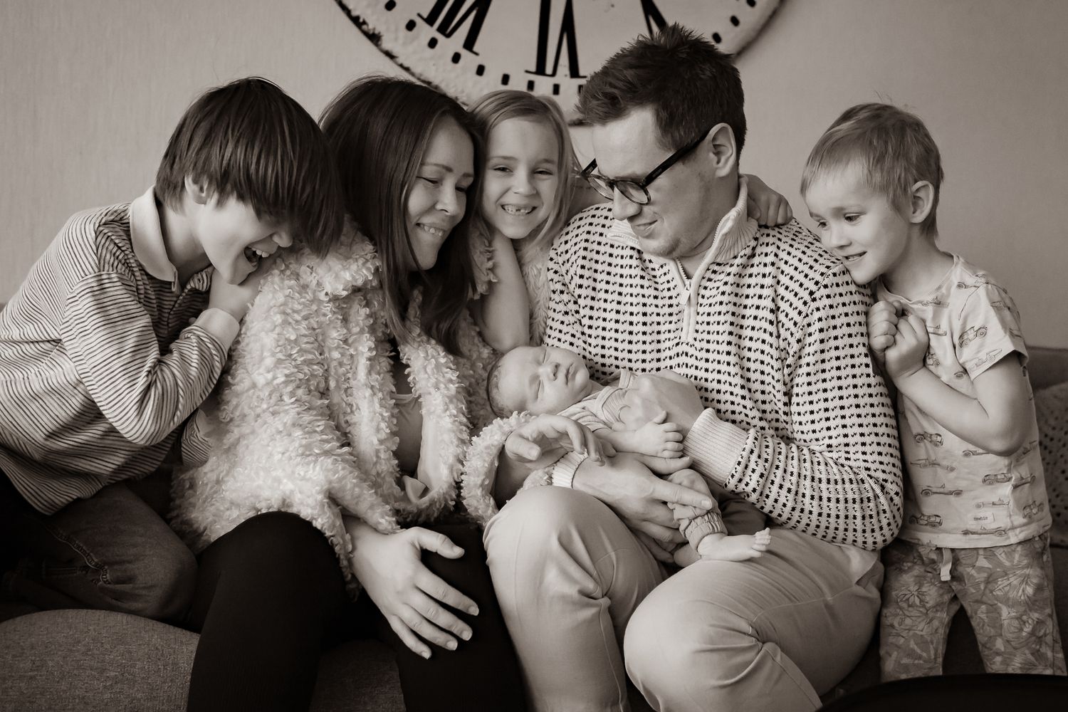 En kärleksfull familj som sitter nära tillsammans i vardagsrumssoffan med en bebis i centrum. Fotograf, familjefotograf, Umeå, Västerbotten
