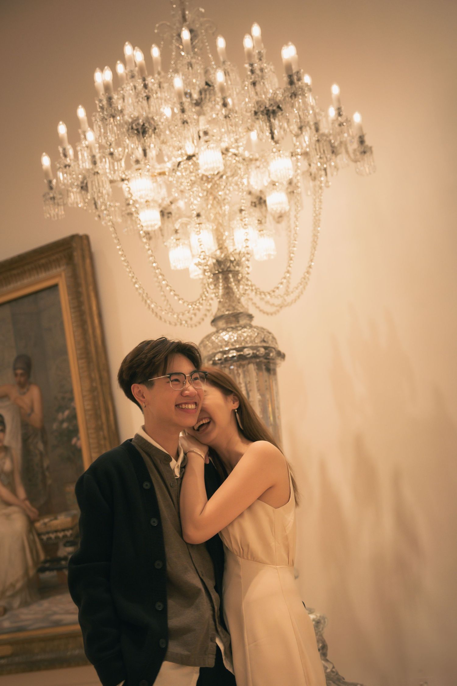 A couple shares a romantic moment under a crystal chandelier in warm lighting.