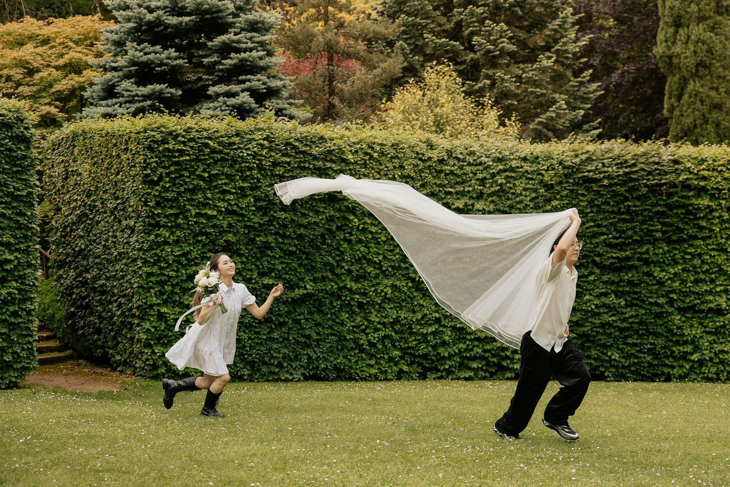 A couple dances playfully on a lush green lawn with flowing white fabric creating graceful movement in the scene.
