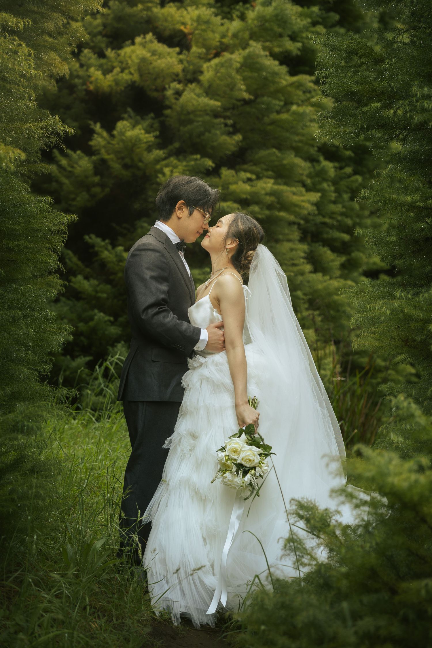 A romantic wedding couple shares an intimate moment in a lush garden setting with greenery in the background.