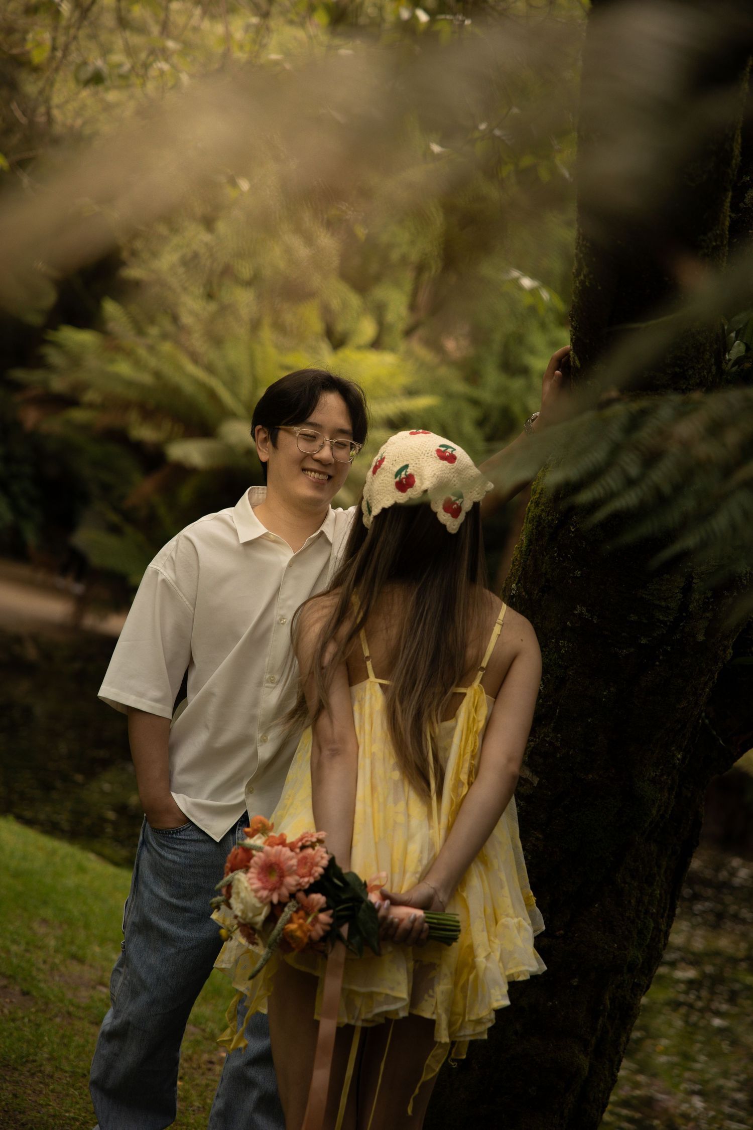 A couple shares a tender moment in a lush garden setting with natural lighting and foliage in the background.