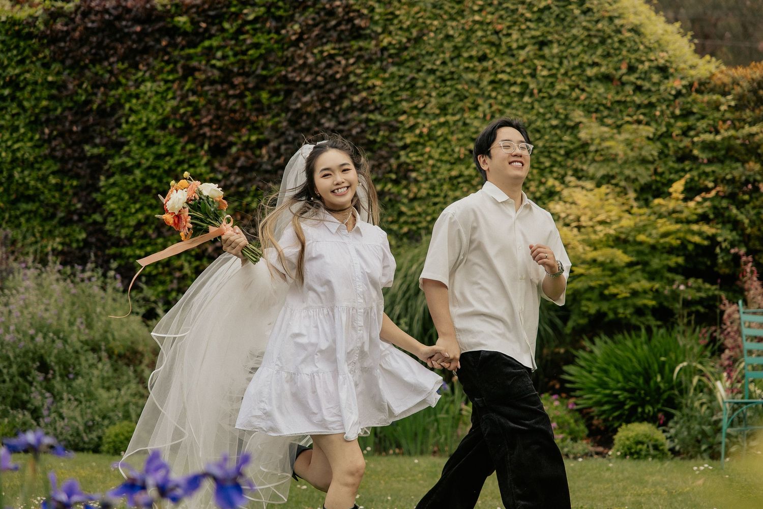 A couple in wedding attire dances joyfully together in a lush garden setting during their outdoor celebration.