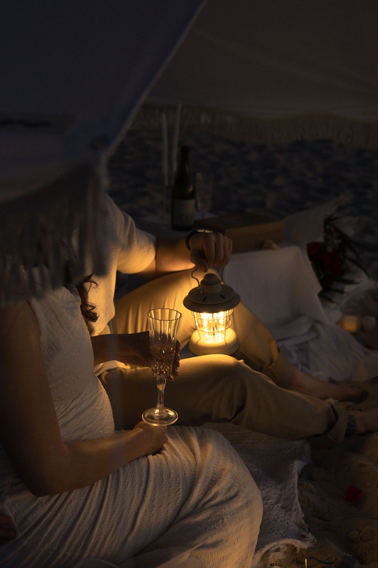 A cozy evening scene with glowing lantern light illuminating someone relaxing with a glass of wine in bed.