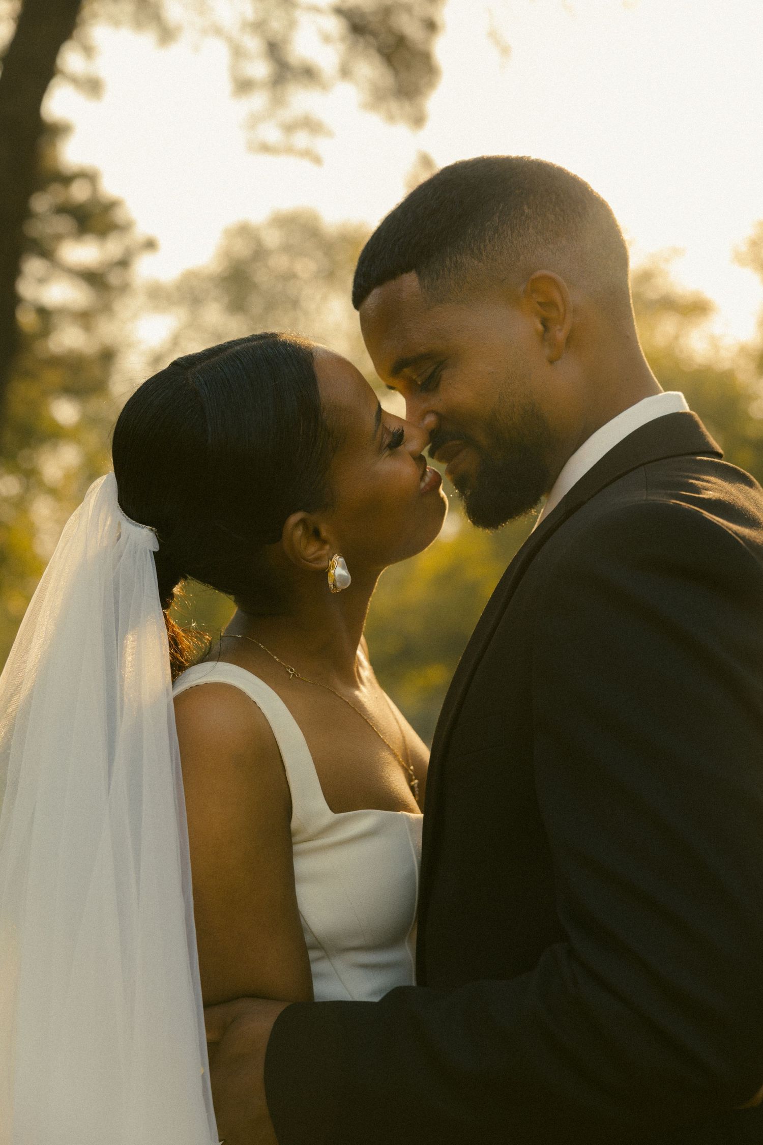 A romantic silhouetted couple in wedding attire share an intimate kiss during golden hour sunset.