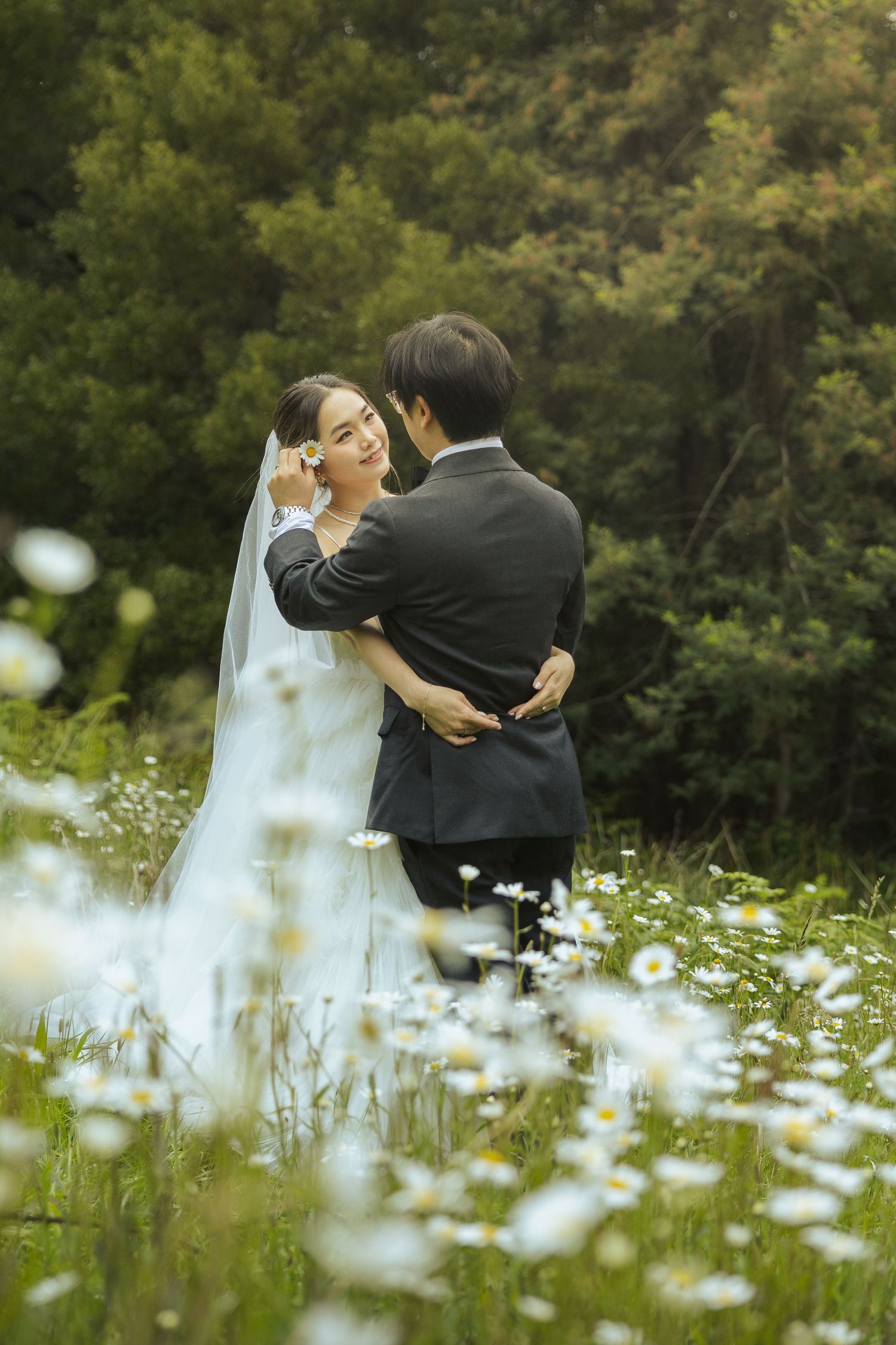 A romantic wedding couple embraces in a field of white daisies during a summer photoshoot.