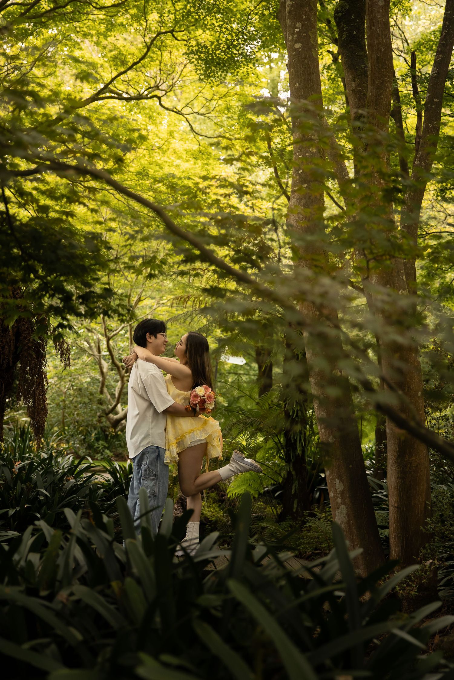 A romantic moment captured in a sunlit forest with golden light filtering through the trees.