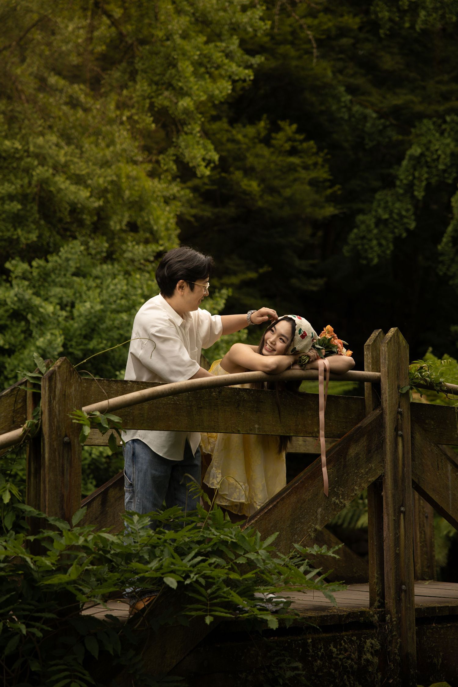 A couple relaxes together on a wooden bridge in a lush garden setting.