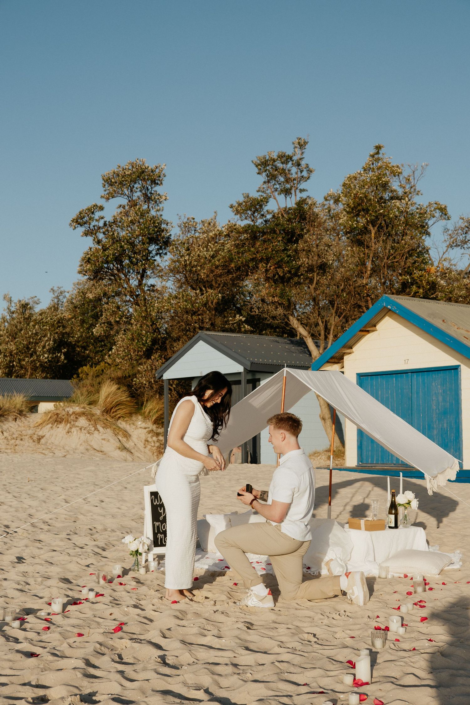 A sequence of beach cabanas in white and blue colors set against sand dunes and trees on a sunny day.