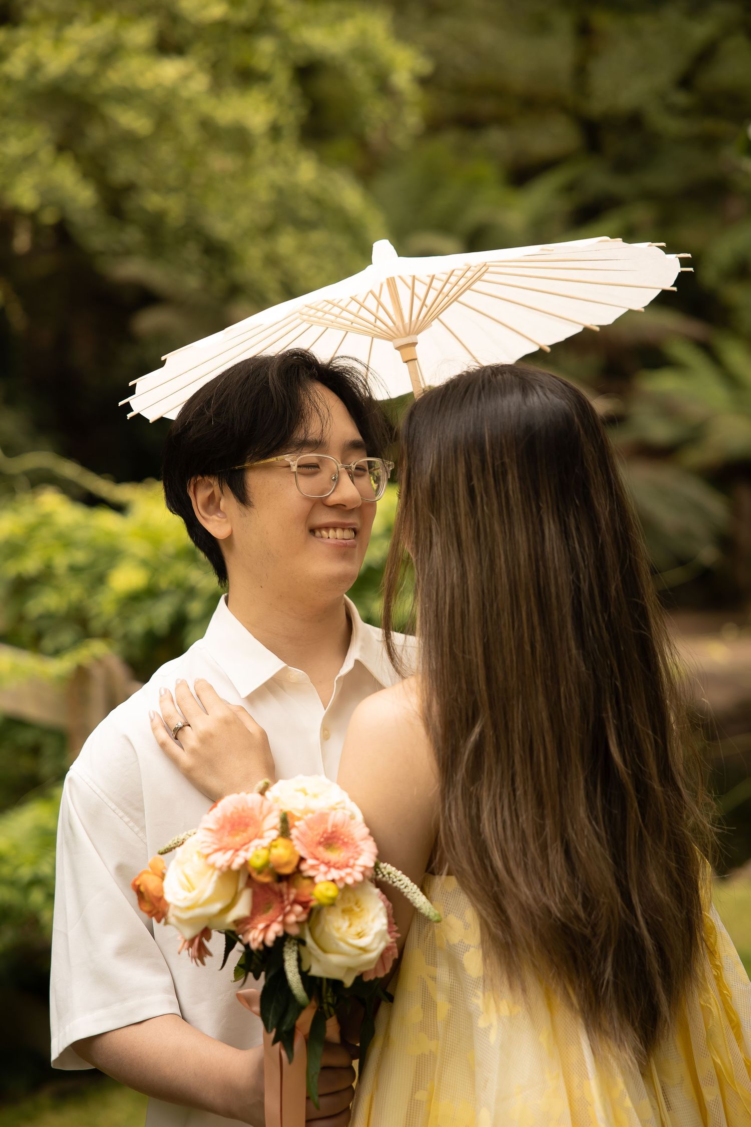 Couple sharing a romantic moment in a garden setting with a decorative parasol and floral bouquet.