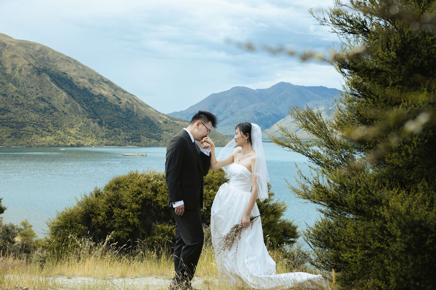 A scenic wedding photoshoot with mountains and a lake in the background on a sunny day.