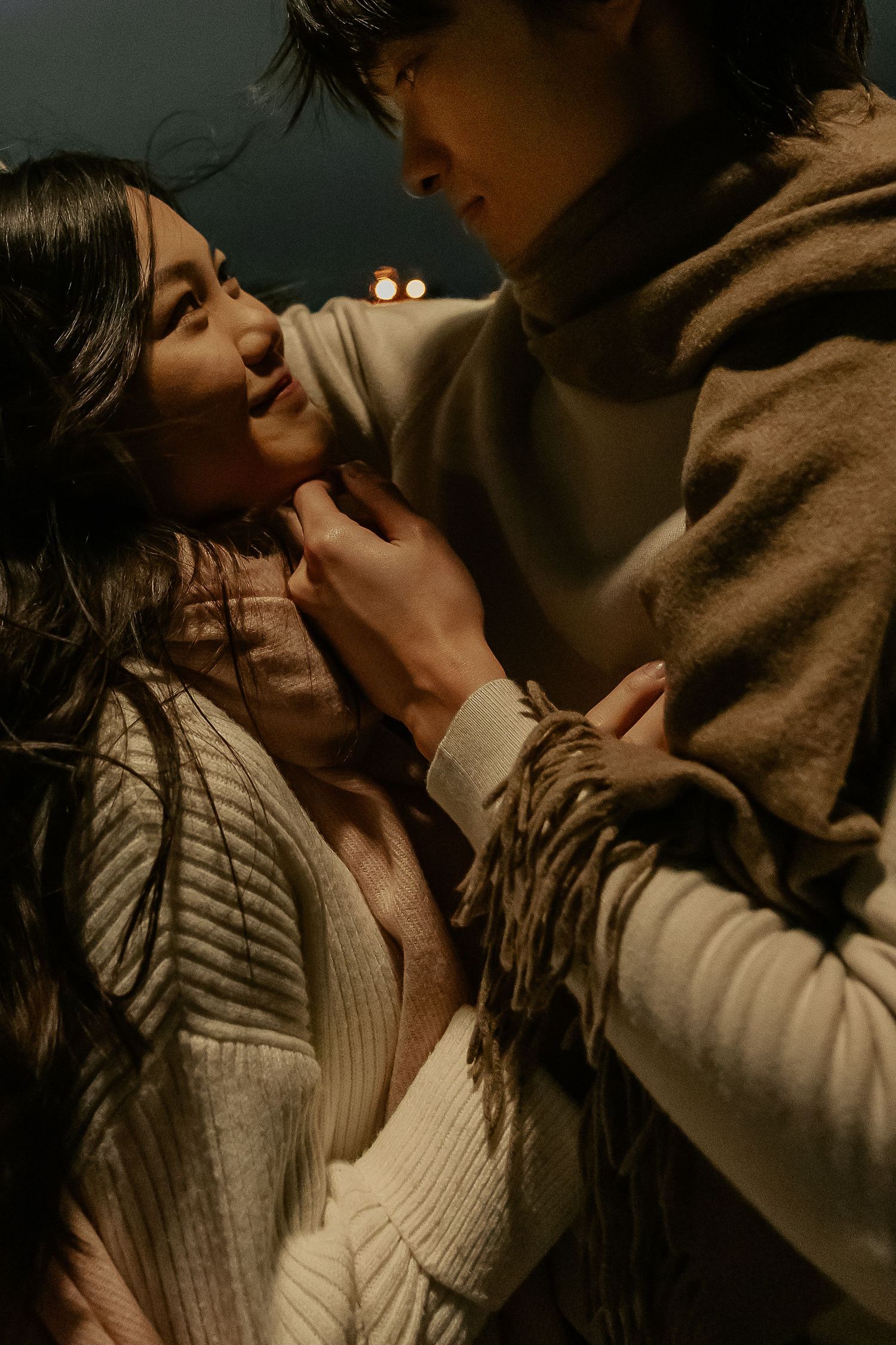A romantic couple embraces intimately in moody lighting while wearing cozy sweaters.